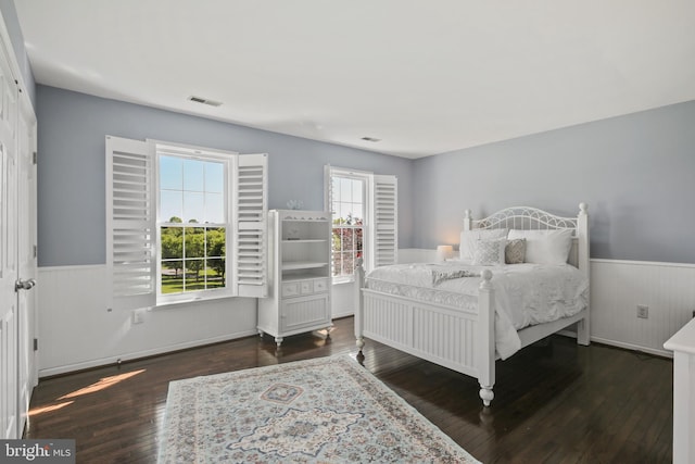 bedroom with visible vents, a wainscoted wall, multiple windows, and wood finished floors
