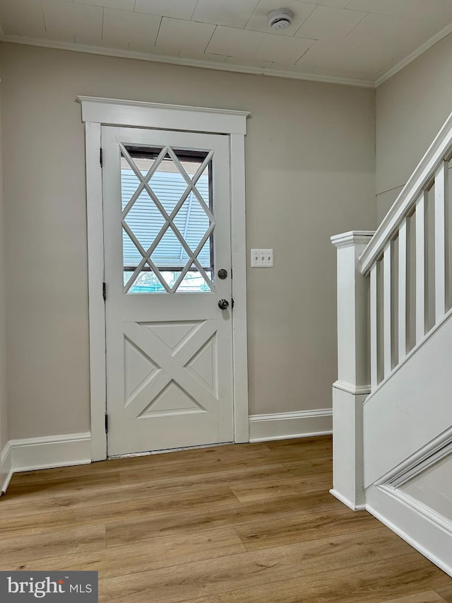 doorway with stairway, light wood-style floors, crown molding, and baseboards