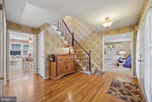 entrance foyer with baseboards, wallpapered walls, stairway, and light wood finished floors