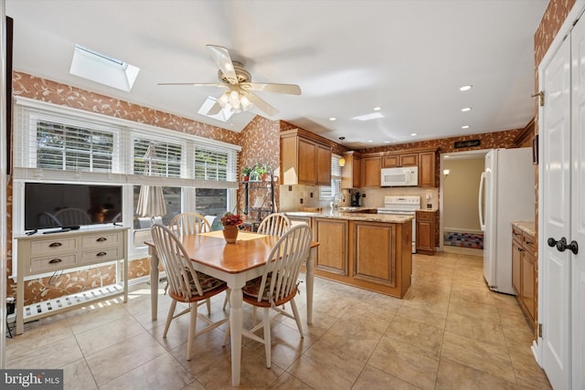 dining room featuring a skylight, a ceiling fan, wallpapered walls, and a healthy amount of sunlight