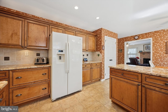 kitchen featuring white fridge with ice dispenser, wallpapered walls, and brown cabinetry