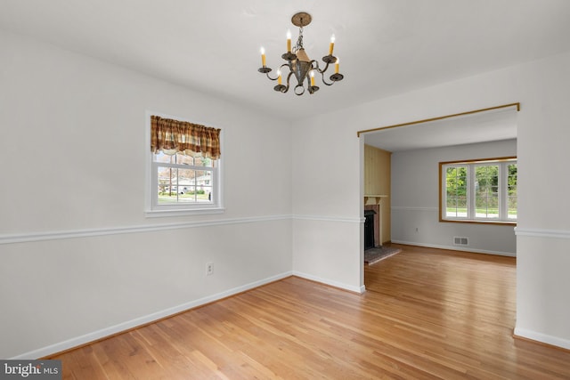 spare room featuring visible vents, a fireplace with raised hearth, baseboards, an inviting chandelier, and light wood finished floors