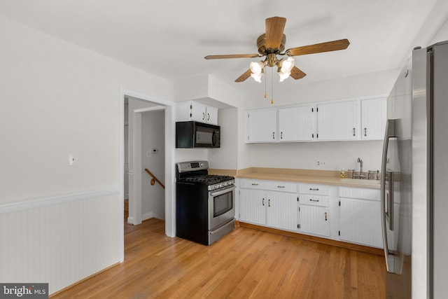 kitchen with white cabinets, a sink, appliances with stainless steel finishes, light countertops, and light wood-type flooring