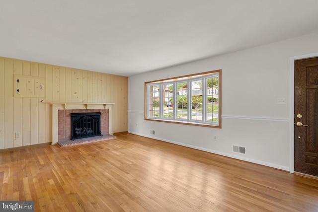 unfurnished living room featuring baseboards, visible vents, light wood-style flooring, and a brick fireplace
