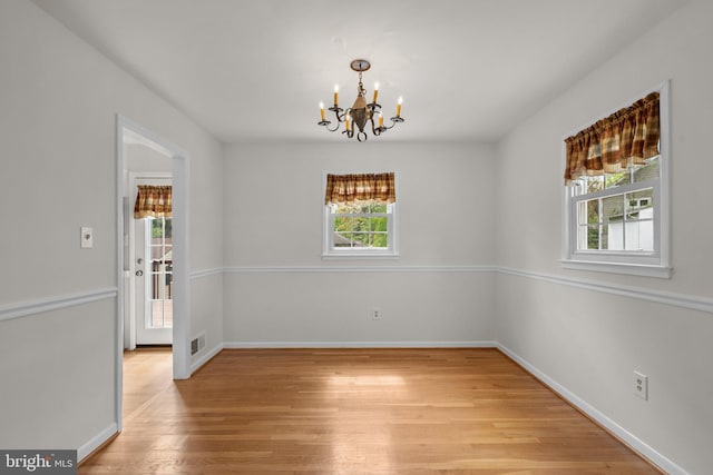 unfurnished dining area with baseboards, visible vents, a notable chandelier, and light wood finished floors