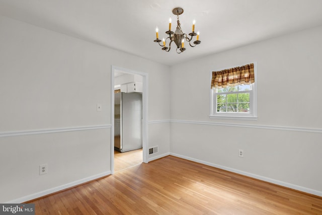 spare room with light wood-style flooring, visible vents, a notable chandelier, and baseboards