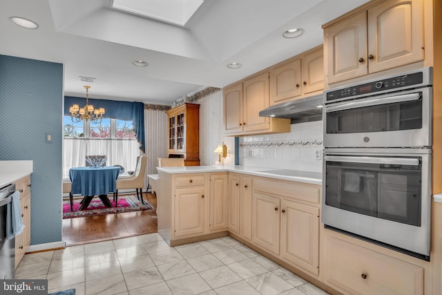 kitchen featuring stainless steel double oven, light countertops, a peninsula, a notable chandelier, and under cabinet range hood