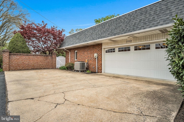 view of side of home featuring cooling unit, roof with shingles, mansard roof, brick siding, and concrete driveway