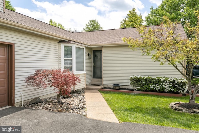 doorway to property featuring a yard and a shingled roof