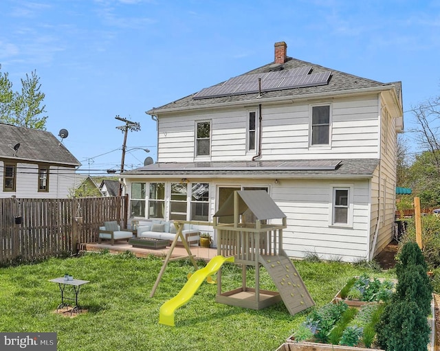 rear view of property featuring a lawn, fence, solar panels, and a playground
