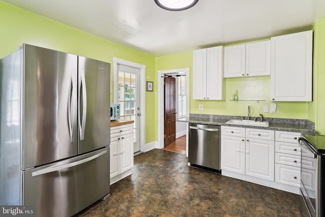 kitchen with a sink, baseboards, white cabinets, dark stone counters, and stainless steel appliances