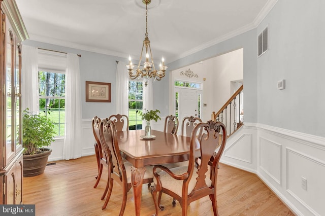 dining area featuring a notable chandelier, light wood finished floors, a decorative wall, a wainscoted wall, and visible vents