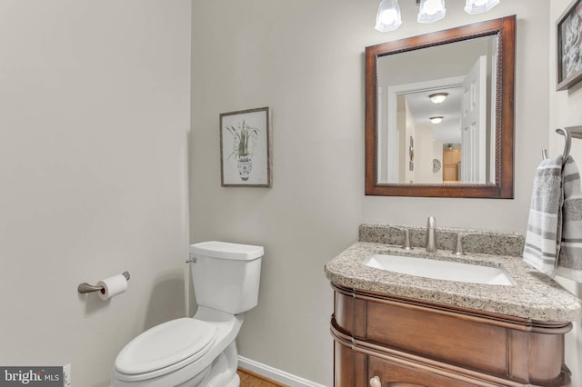half bath with toilet, baseboards, and vanity