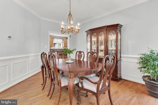 dining room featuring an inviting chandelier, crown molding, wainscoting, and light wood finished floors