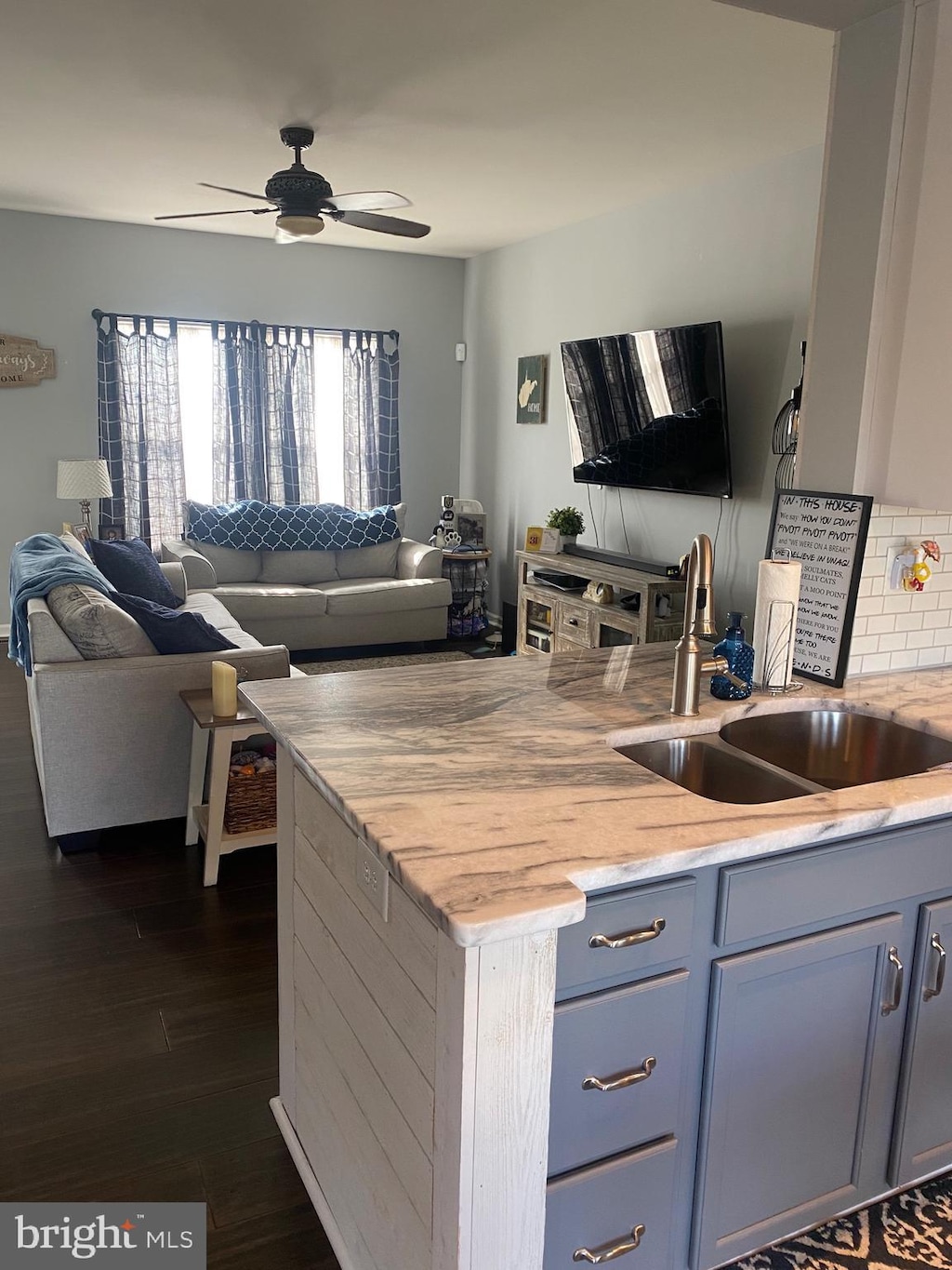 kitchen featuring dark wood-style flooring, open floor plan, ceiling fan, light stone counters, and a sink