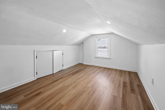 additional living space featuring a textured ceiling, baseboards, wood finished floors, and lofted ceiling