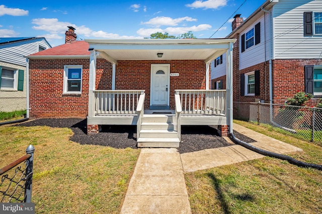 view of front of property with fence, brick siding, a front yard, a chimney, and covered porch