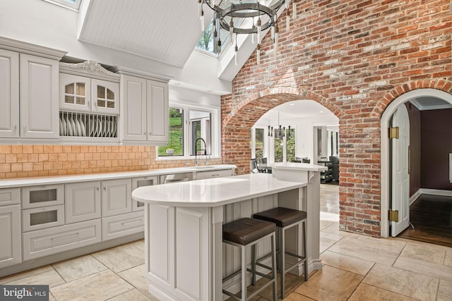 kitchen with a sink, light countertops, arched walkways, a breakfast bar area, and a towering ceiling