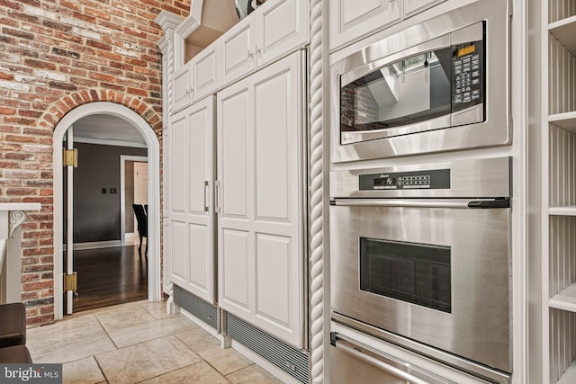 kitchen featuring arched walkways, a fireplace, a warming drawer, stainless steel appliances, and white cabinetry
