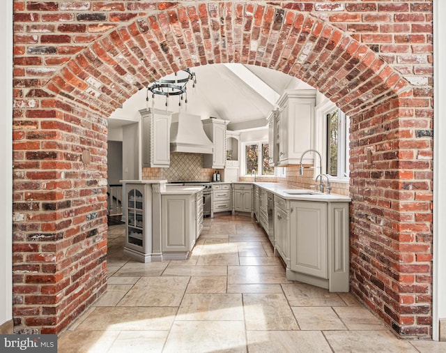 kitchen with a sink, lofted ceiling, tasteful backsplash, custom range hood, and stone tile flooring