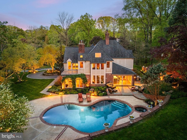 back of house with an in ground hot tub, a chimney, a balcony, a yard, and a patio