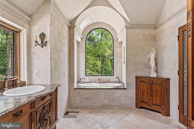 bathroom with vanity, stone tile floors, tile walls, lofted ceiling, and a garden tub