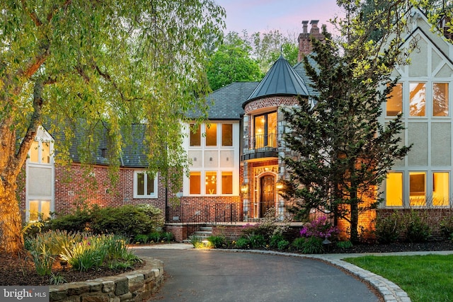 tudor house with a balcony, stucco siding, a chimney, a standing seam roof, and brick siding