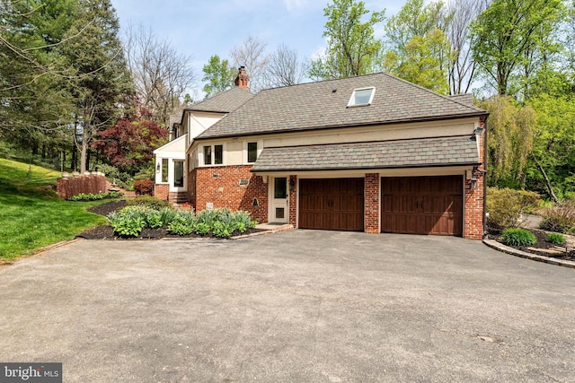 view of front of home featuring an attached garage, a chimney, aphalt driveway, and brick siding