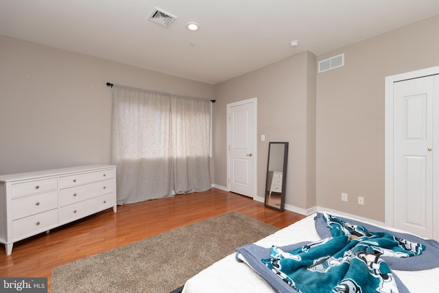 bedroom with baseboards, visible vents, and wood finished floors