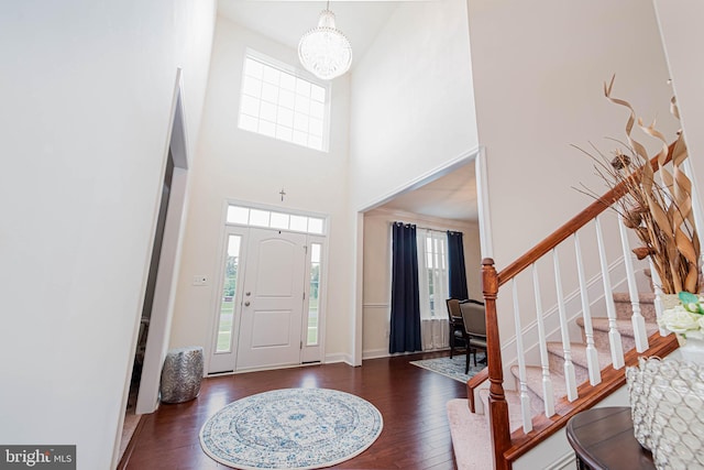 foyer with wood finished floors, stairway, an inviting chandelier, a high ceiling, and baseboards