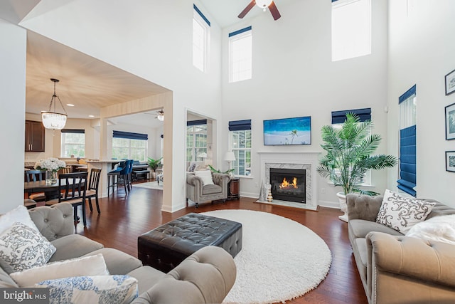 living area featuring a fireplace, a ceiling fan, dark wood-style floors, a high ceiling, and baseboards