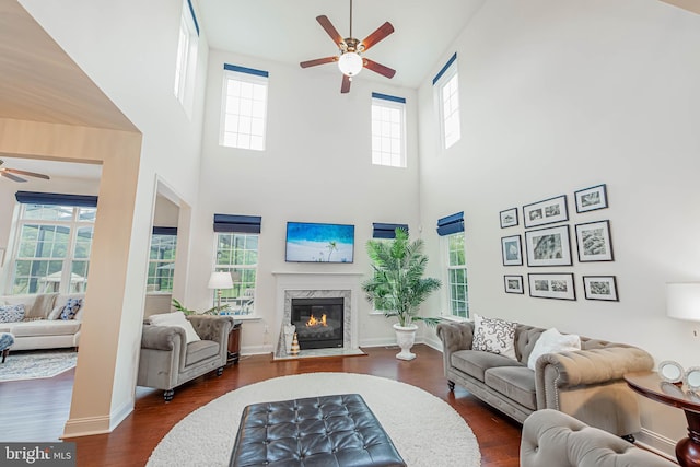 living area with a premium fireplace, ceiling fan, a towering ceiling, and dark wood-style flooring