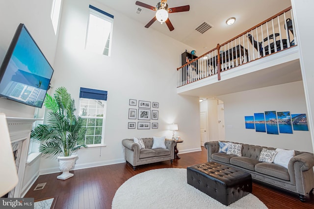 living area featuring a high ceiling, wood-type flooring, visible vents, baseboards, and ceiling fan
