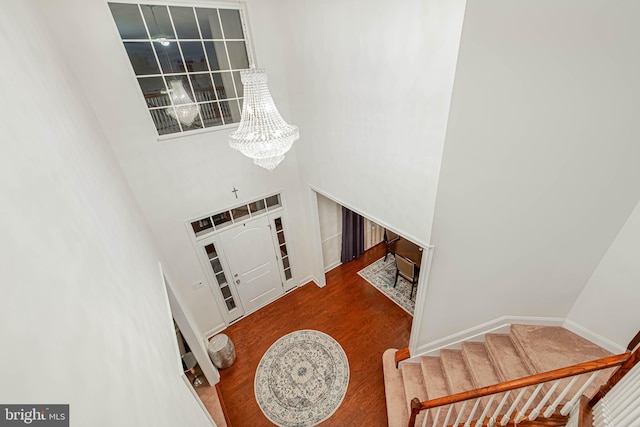foyer entrance featuring wood finished floors, baseboards, stairway, a high ceiling, and a notable chandelier