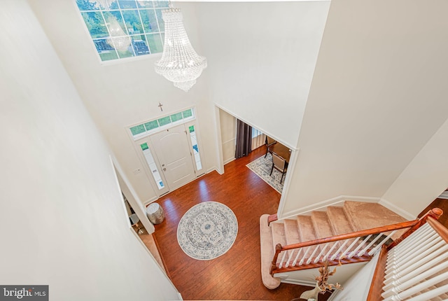 foyer entrance featuring baseboards, an inviting chandelier, a towering ceiling, wood finished floors, and stairway