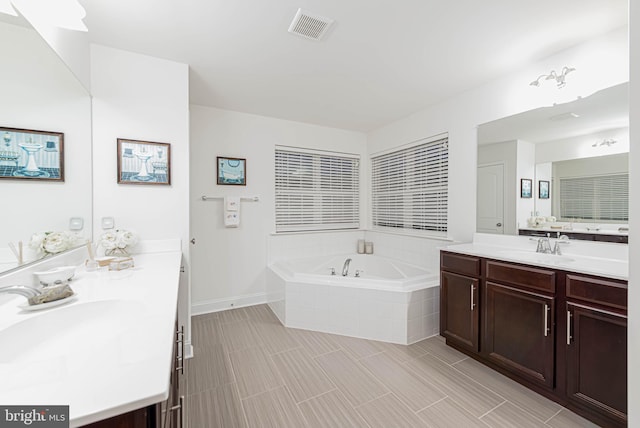 bathroom featuring a bath, visible vents, two vanities, and a sink