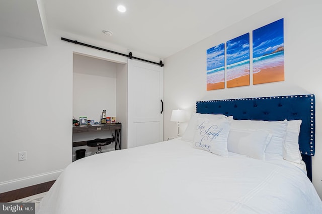 bedroom featuring wood finished floors, a barn door, and baseboards
