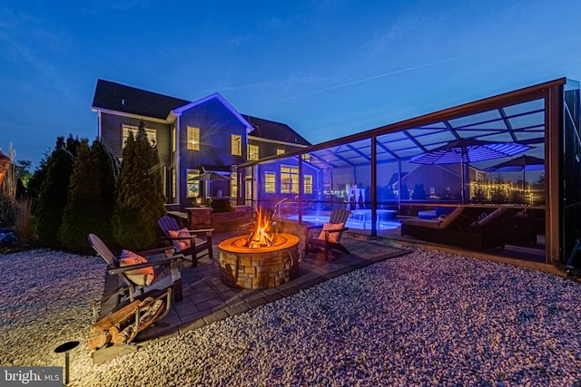 patio at night with a fire pit, a lanai, and an outdoor pool
