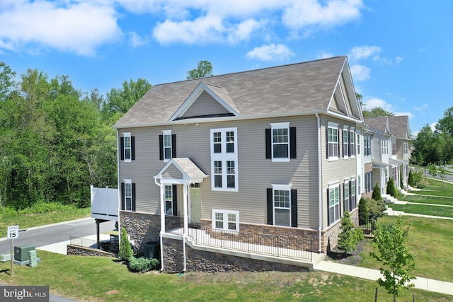 view of front facade with roof with shingles, central AC, a front yard, and stone siding