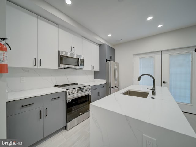 kitchen with recessed lighting, a sink, appliances with stainless steel finishes, backsplash, and gray cabinetry