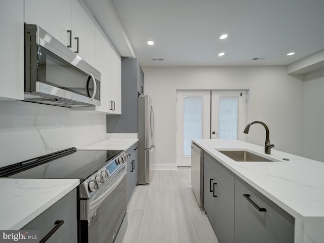 kitchen with a sink, gray cabinets, light stone countertops, and stainless steel appliances