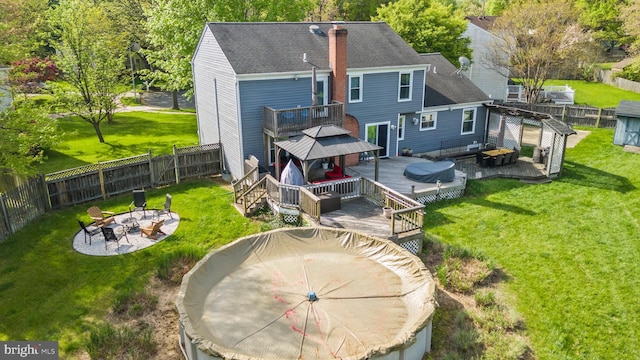 back of property with an outdoor fire pit, a fenced backyard, a chimney, a deck, and a gazebo