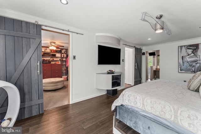 bedroom featuring dark wood finished floors, a barn door, a spacious closet, and crown molding