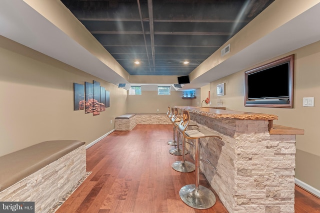 interior space with visible vents, hardwood / wood-style flooring, indoor wet bar, and baseboards