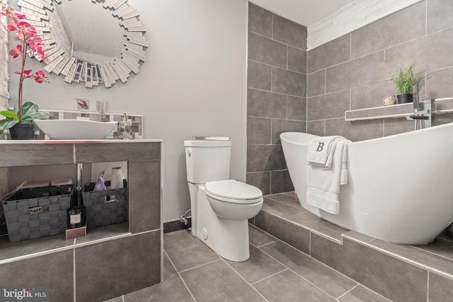 full bath with toilet, a sink, tile patterned flooring, and a freestanding bath