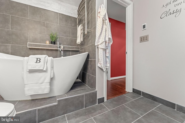 bathroom featuring a soaking tub, baseboards, toilet, tile walls, and tile patterned floors