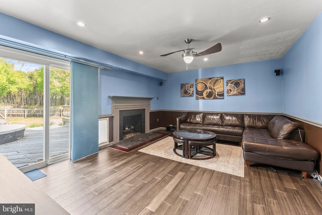 living room featuring wainscoting, wood finished floors, ceiling fan, and a brick fireplace