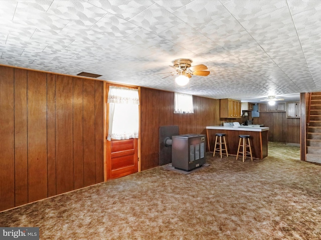interior space with brown cabinets, a breakfast bar, a wood stove, wood walls, and carpet