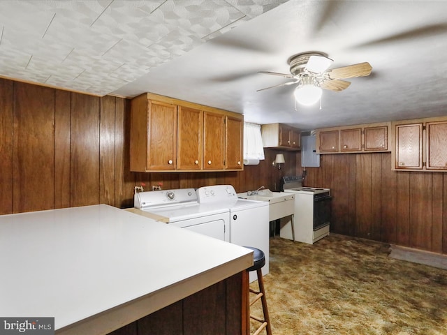 laundry area featuring washer and dryer, dark carpet, ceiling fan, wooden walls, and a sink