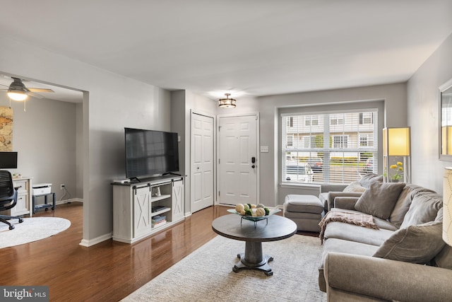 living area featuring a ceiling fan, baseboards, and dark wood-type flooring